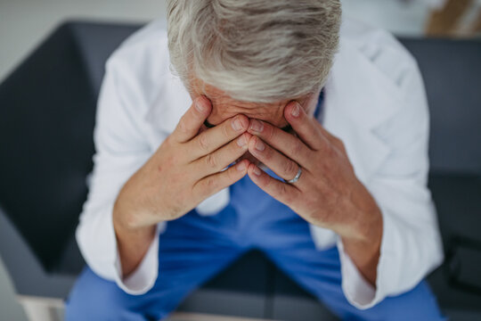 High angle shot of frustrated, exhausted doctor sitting in hospital corridor. Concept of burnout syndrome among doctors.