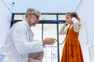 Obraz premium Little girl listening to the doctor's heart with stethoscope. Role reversal. Friendly relationship between the doctor and child patient.
