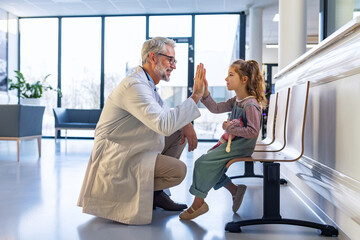 Friendly pediatrician giving high five to little patient. Cute preschool girl in greeting doctor in...