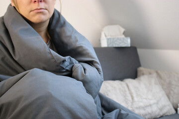 Sick woman sitting on sofa with blanket, blurry background