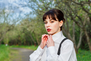 A beautiful girl in a white shirt, in black trousers with suspenders against the background of the sky and green grass