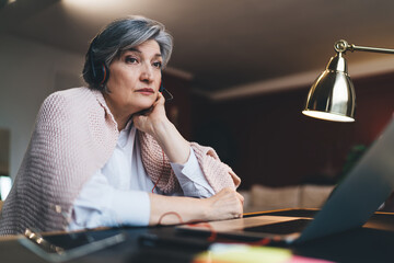 Tired mature woman working on laptop in dark room