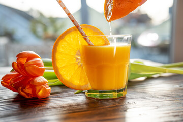 Glass freshly squeezed orange juice with a slice of orange and a bouquet of tulips on a wooden table. Close-up with short depth of field. - 709753214