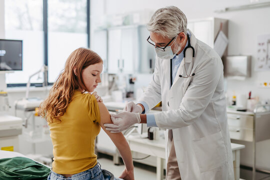 Doctor, pediatrician injecting vaccine into teenage girl arm. Concept of preventive health care for adolescents.