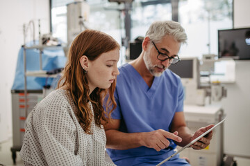 Obraz premium Doctor showing teenage patient MRI scan on tablet, discussing test result in emergency room.
