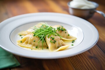 plate of boiled polish pierogi with sour cream and chives