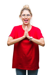Young beautiful blonde woman wearing red t-shirt and glasses over isolated background begging and praying with hands together with hope expression on face very emotional and worried.