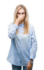 Young beautiful blonde business woman wearing glasses over isolated background smelling something...