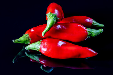 Five ripe red chili peppers isolated on a black reflecting background