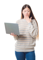 Young Chinese woman over isolated background using computer laptop cover mouth with hand shocked with shame for mistake, expression of fear, scared in silence, secret concept