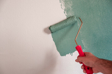 Repairman painting white wall in apartment green using roller, closeup