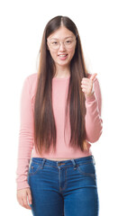 Young Chinese woman over isolated background wearing glasses doing happy thumbs up gesture with hand. Approving expression looking at the camera with showing success.