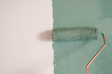Repairman painting white wall in apartment green using roller, closeup
