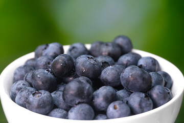 Close-up of a white bowl with blueberries on a blurry green background, macro photography