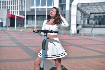 Naklejka premium Basking in sunlight. A glamorous young adult model in an elegant white outfit, strikes a graceful pose with closed eyes on an electric scooter against of a modern city on a radiant sunny day