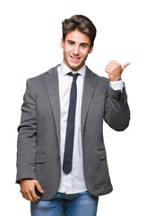 Young business man wearing suit and tie over isolated background smiling with happy face looking and pointing to the side with thumb up.