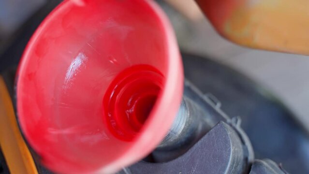 Fuel is poured into the lawn mower tank until it is full through a funnel. Hand tightens the gas tank cap, close-up