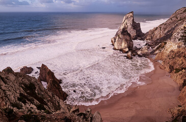 Portugal Ursa Beach at сoast of Atlantic Ocean. Rocks and waves at sand of coastline picturesque...