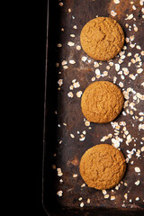 Craft and rustic four oatmeal cookies. Dark food aesthetics, black background with several oat flakes.