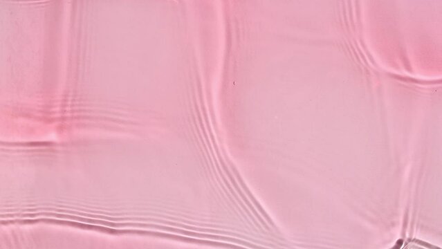 Pure pink water with reflections sunlight in slow motion. Water surface texture. Sun and shadows. Motion clean swimming pool ripples and wave. High quality 4k footage. High quality 4k footage