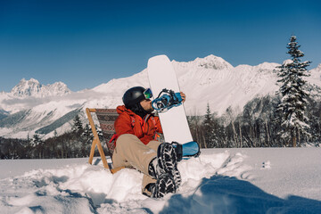 Resting snowboarder kiss his snowboard sitting in chair on powder snow at ski resort