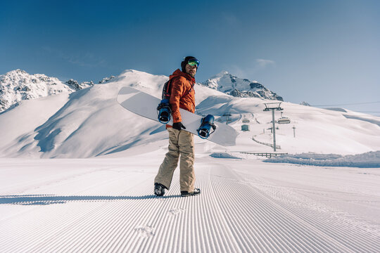 snowboarder holding snowboard walking along ski slope at  resort prepared by snowcat