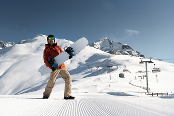 snowboarder holding snowboard standing and posing along ski slope at  resort prepared by snowcat