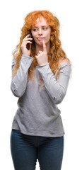 Young redhead woman talking on the phone serious face thinking about question, very confused idea