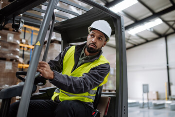 Portrait of warehouse worker driving forklift. Warehouse worker preparing products for shipmennt,...