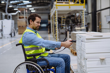 Portrait of man in wheelchair working in modern industrial factory, scanning with scanner. Concept of workers with disabilities, accessible workplace for employees with mobility impairment.