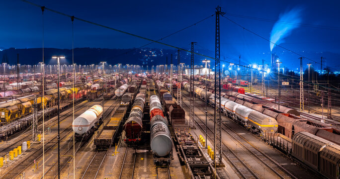 Panoramic view of large shunting yard and freight station in Hagen Germany on a cold winters night. Brightly illuminated colorful infrastructure with trains, cars and wagons an many parallel tracks.
