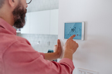 Man using smart thermostat, adjusting, lowering heating temperature at home. Concept of...