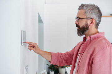 Man using smart thermostat, adjusting, lowering heating temperature at home. Concept of...