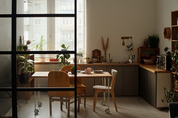 Part of spacious kitchen with counter, group of chairs, wooden table with kitchenware and green...