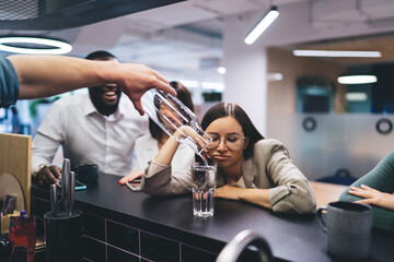 Office barman pouring water into glass for overworked female employee