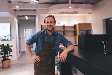 Smiling male barista leaning on counter in office
