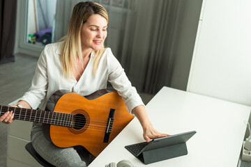 Woman artist playing the guitar and live or stream on laptop in the living room, Relaxation with...
