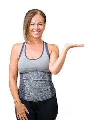 Fototapeta premium Beautiful middle age woman wearing sport clothes over isolated background smiling cheerful presenting and pointing with palm of hand looking at the camera.