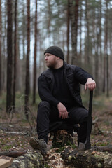 A bearded forester is resting near a felled diseased tree covered with fungus and moss. Sanitary logging of a forest or park. Late autumn or winter.