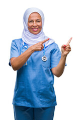 Middle age senior arab nurse woman wearing hijab over isolated background smiling and looking at the camera pointing with two hands and fingers to the side.