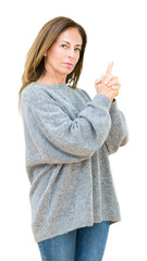 Beautiful middle age woman wearing winter sweater over isolated background Holding symbolic gun with hand gesture, playing killing shooting weapons, angry face