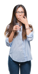 Young asian woman drinking a glass of water over isolated background cover mouth with hand shocked with shame for mistake, expression of fear, scared in silence, secret concept