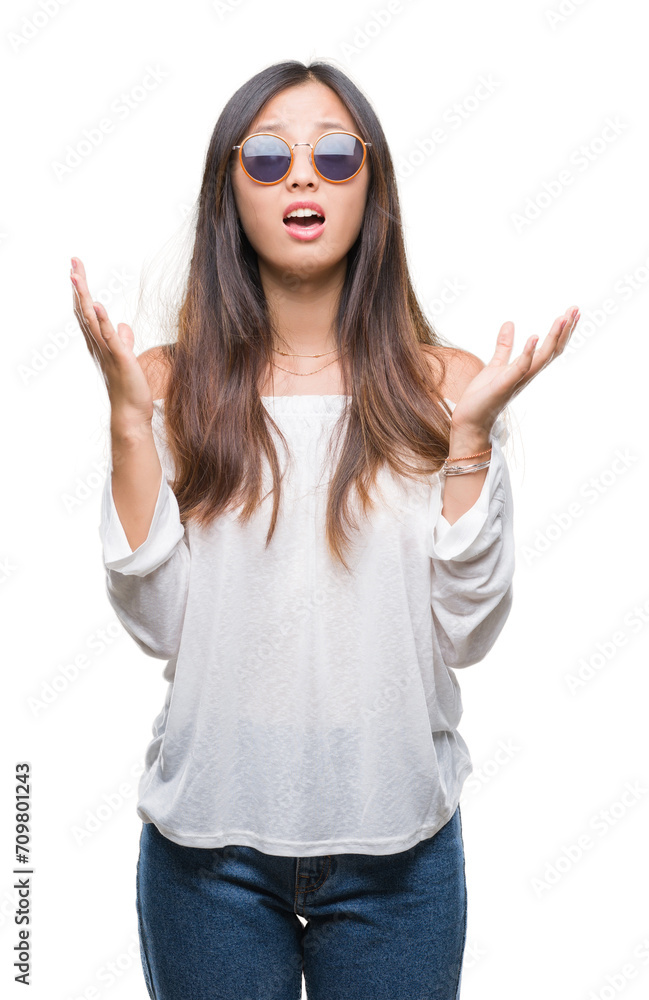 Sticker young asian woman wearing sunglasses over isolated background crazy and mad shouting and yelling wit