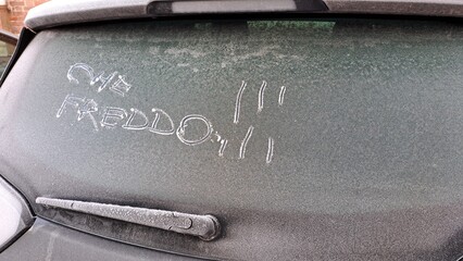 Che freddo ! scritta italiano sul lunotto posteriore di un'auto coperta da ghiaccio.