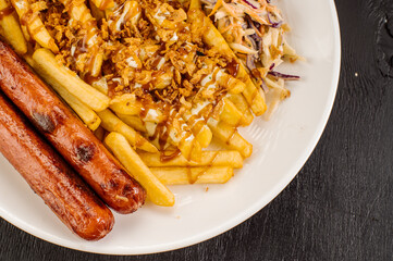 A dish of French fries with bacon, cheese sauce and sausages on a plate