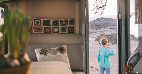 Woman from behind with a blue shirt outside the camper looking at the panorama that surrounds her....