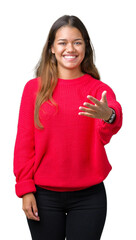 Young beautiful brunette woman wearing red winter sweater over isolated background smiling friendly offering handshake as greeting and welcoming. Successful business.