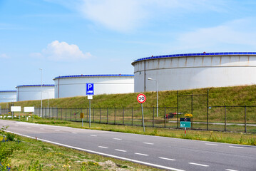Fenced oil terminal with large tanks for crude oil storage at a port on a sunny summer day