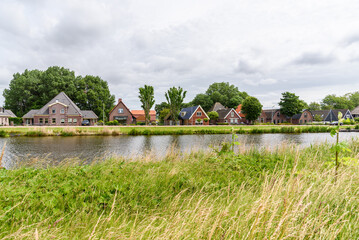 Brick houses along a canal in the countryside of Netherlands on a cloudy summer day