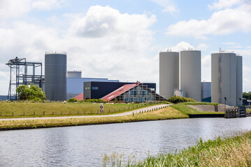 Factory with storage tanks and silos along a canal on partly cloudy summer day